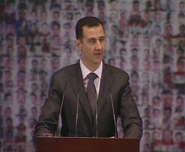 Prezydent al-Asad przemawia na tle flagi utworzonej ze zdjęć twarzy - Fot. Reuters.