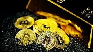 Model Bitcoinów obok sztabki złota.