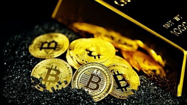 Model Bitcoinów obok sztabki złota.