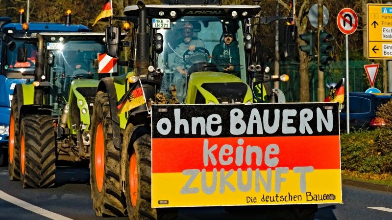 Traktory podczas protestu z transparentem w kolorach flagi Niemiec i napisem