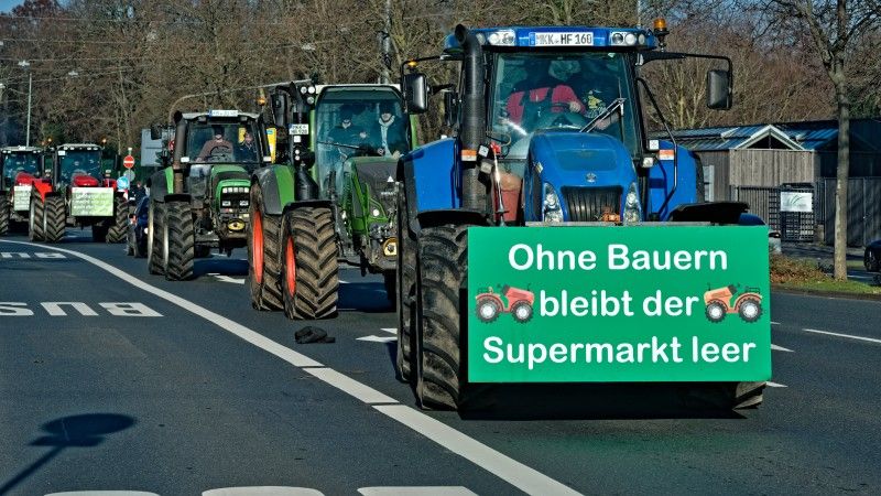 Rząd traktorów blokujących ulicę, na jednym z nich wywieszono transparent z napisem: „bez rolników supermarkety pozostają puste”