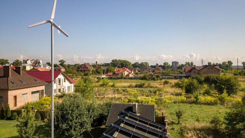Widok na osiedle domów jednorodzinnych z panelami słonecznymi i mini wiatrakiem w ogrodzie