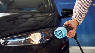 Mężczyzna trzyma wtyczkę do ładowania samochodu elektrycznego. W tyle czarny samochód