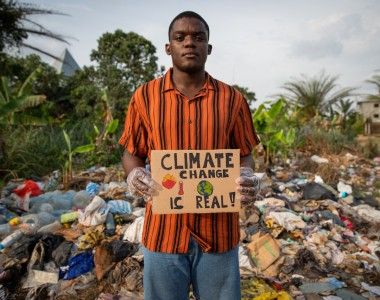 Chłopak trzyma tabliczkę z napisem „climate change is real”, stoi na tle wysypiska śmieci
