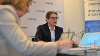 Sławomir Hinc siedzący przy stole na tle ścianki Gaz-System