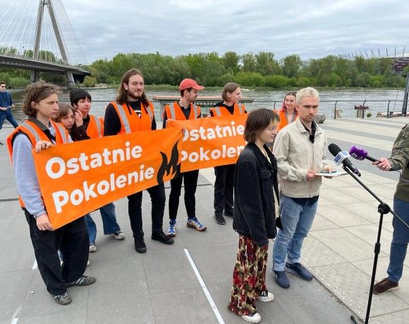 grupa aktywistów trzyma dwa transparenty z napisem „Ostatnie Pokolenie” przy moście nad Wisłą. Dwoje wypowiada się do mikrofonów mediów