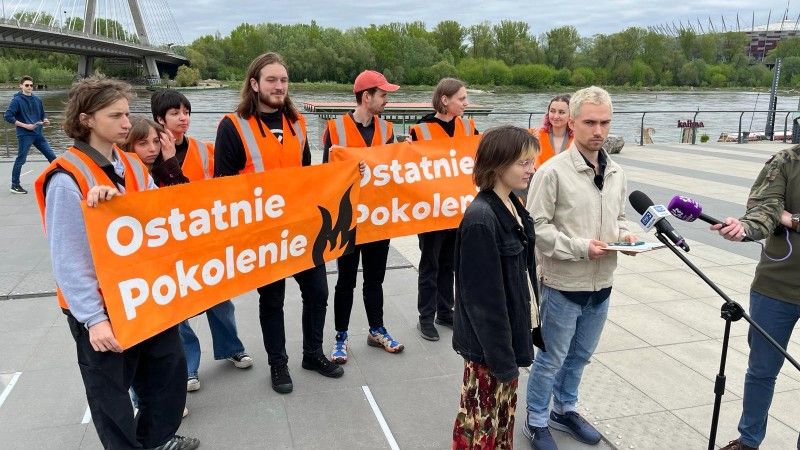 grupa aktywistów trzyma dwa transparenty z napisem „Ostatnie Pokolenie” przy moście nad Wisłą. Dwoje wypowiada się do mikrofonów mediów