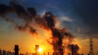 Widok na fabrykę, z której kominów leci dym, o zachodzie słońca