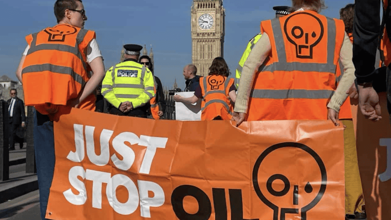 aktywiści w kamizelkach just stop oil trzymają pomarańczowy transparent na ulicy przed Big Benem
