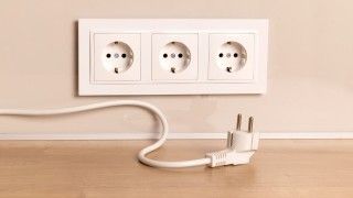 Trzy gniazdka na ścianie z wyciągniętą wtyczką leżącą na podłodze