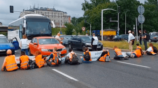 Aktywiści siedzą na ulicy z transparentami