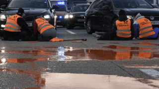 aktywiści w pomarańczowych kamizelkach Letzte Generation blokują ulicę