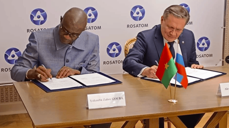 Mężczyźni podpisują dokumenty przy stole. W tle ścianka z logiem Rosatomu