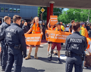 Aktywiści Ostatniego Pokolenia z pomarańczowymi transparentami protestują na ulicy, są otoczeni przez niemiecką policję
