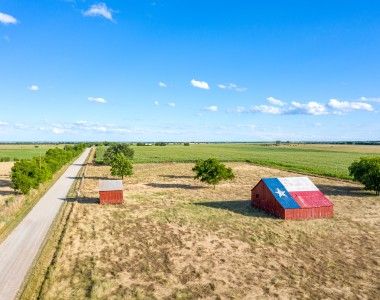 Stodoła z namalowaną na dachu flagą Teksasu, krajobraz wiejski, w tle pola i pojedyczna droga