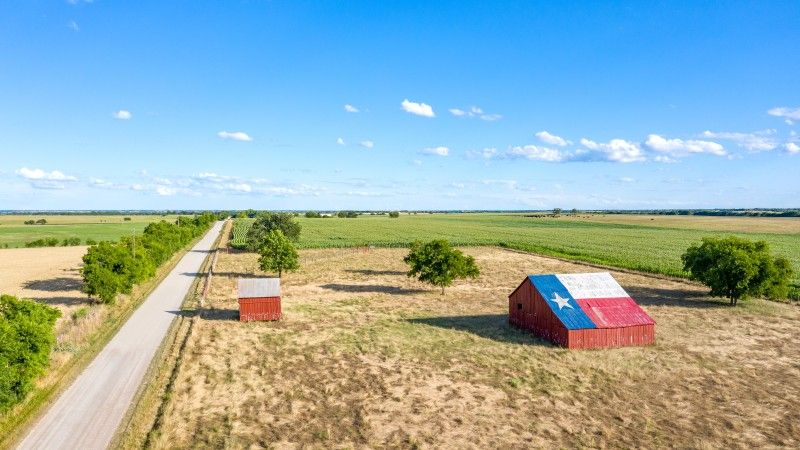 Stodoła z namalowaną na dachu flagą Teksasu, krajobraz wiejski, w tle pola i pojedyczna droga