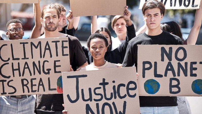 Ludzie na proteście trzymają kartony z napisami: climate change is real, justice now, no planet b