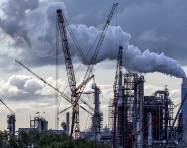 Dymiące kominy, wiatraki, zbiorniki i dźwigi na tle nieba. Bardzo industrialny krajobraz
