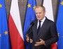 Premier Donald Tusk przemawia do mikrofonu na tle flag Polski i UE