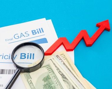 rachunki za prąd i gaz, na nich leżą banknoty i lupa. obok narysowana jest strzałka oznaczająca wzrost