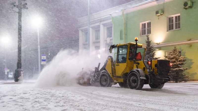 Żółty traktor odśnieża ulicę w nocy