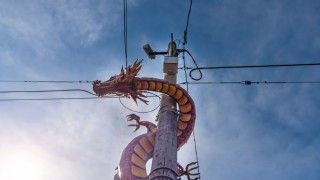 Czerwony chiński smok wspina się po słupie elektrycznym na tle błękitnego nieba.
