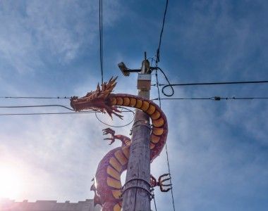 Czerwony chiński smok wspina się po słupie elektrycznym na tle błękitnego nieba.