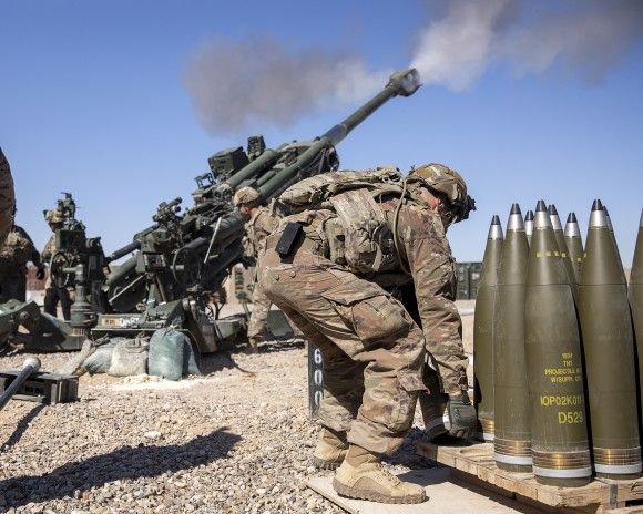 Artylerzyści 25 Dywizji Piechoty U.S. Army prowadzą ogień z haubicy M777 na ćwiczeniach w Iraku, marzec 2020 roku. Po prawej widać paletę z pociskami odłamkowo-burzącymi typu M795.