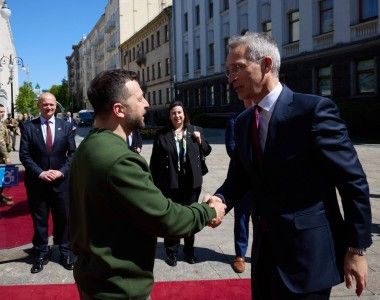 Prezydent Ukrainy Wołodymyr Zełenski i minister finansów Norwegii Jens Stoltenberg ściskają sobie ręce na dworze, świeci słońce