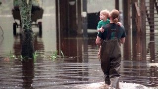 Dziecko przenoszone przez ratownika przez zalany w wyniku powodzi teren.
