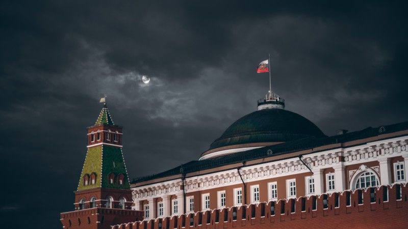 Widok na kopułę Pałacu Senackiego na Kremlu nocą z powiewającą rosyjską flagą.