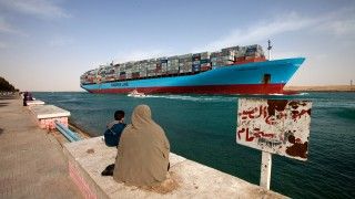 Kobieta w chuście i dziecko obserwują statek handlowy na Kanale Sueskim.