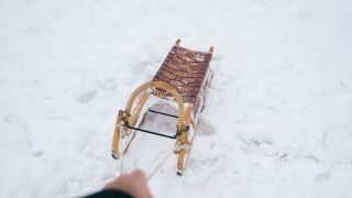Osoba (widać samą dłoń) ciągnie drewniane sanki po śniegu)