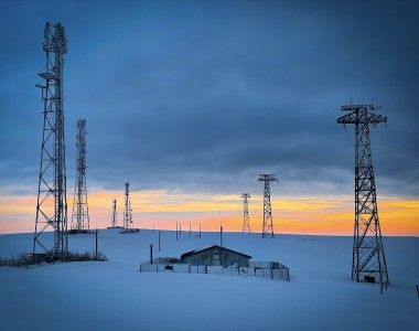 Sieci elektroenergetyczne nad małą samotną chatką zimą o zachodzie słońca, wszystko przykryte grubą warstwą śniegu