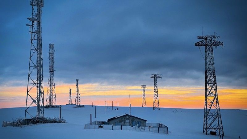 Sieci elektroenergetyczne nad małą samotną chatką zimą o zachodzie słońca, wszystko przykryte grubą warstwą śniegu