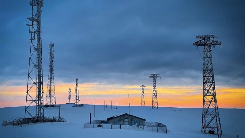 Sieci elektroenergetyczne nad małą samotną chatką zimą o zachodzie słońca, wszystko przykryte grubą warstwą śniegu
