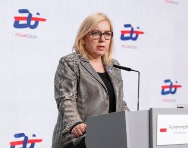 Ministra stoi przy mównicy na tle ścianki z logo polskiej prezydencji i napisem POLAND25.EU, mówi do mikrofonu