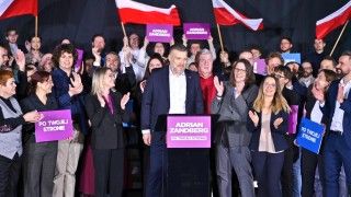 Adrian Zandberg pozuje z członkami partii Razem, niektórzy trzymają flagi Polski i banery z hasłami Razem