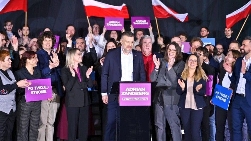 Adrian Zandberg pozuje z członkami partii Razem, niektórzy trzymają flagi Polski i banery z hasłami Razem