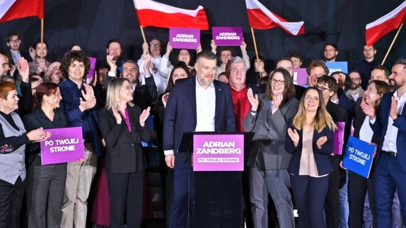 Adrian Zandberg pozuje z członkami partii Razem, niektórzy trzymają flagi Polski i banery z hasłami Razem