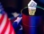 Baryłka ropy stoi na fladze USA. Z baryłki wystaje amerykański dolar