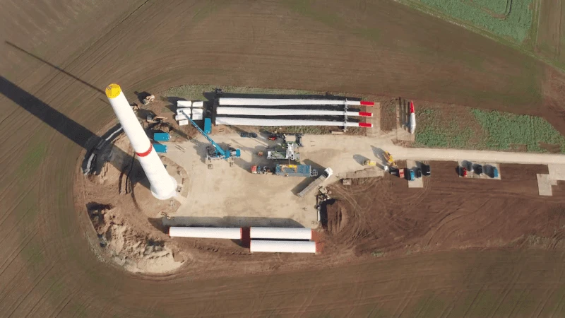Kadr z budowy lądowej turbiny wiatrowej z lotu ptaka – stawiana wieża stalowa