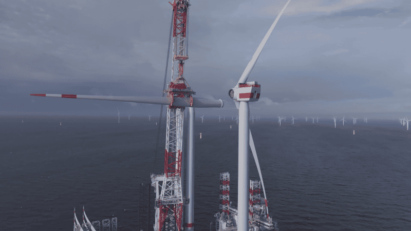 budowa morskiej farmy wiatrowej, dźwig podnosi łopatę wiatraka, na stalowej wieży są już zamocowane dwie, w tle stoi już wiele turbin