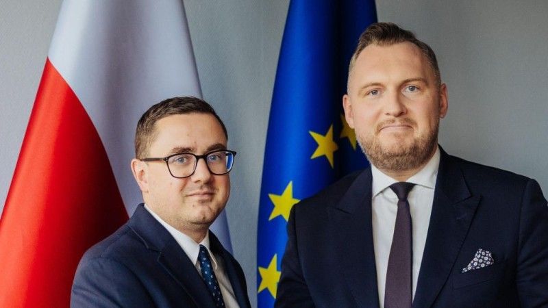 Ministrowie stoją na tle flagi Polski i flagi UE