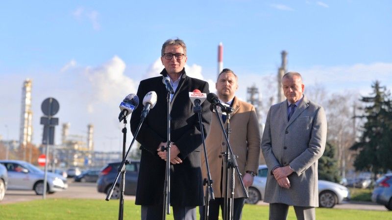 Prezes mówi do mikrofonu na tle kominów przemysłowych