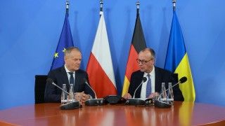 mężczyźni siedzą za stołem, mówią do mikrofonów, w tle flagi UE, Polski, Niemiec i Ukrainy