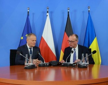 mężczyźni siedzą za stołem, mówią do mikrofonów, w tle flagi UE, Polski, Niemiec i Ukrainy