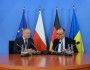 mężczyźni siedzą za stołem, mówią do mikrofonów, w tle flagi UE, Polski, Niemiec i Ukrainy