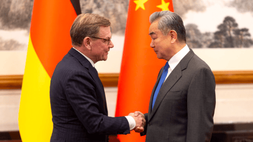 Mężczyźni ściskają sobie ręce, w tle flagi Niemiec i Chin