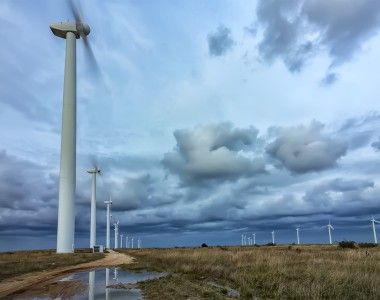 turbiny wiatrowe na silnym wietrze, śmigła obracają się tak szybko że są zamazane, na ziemi są kałuże po burzy